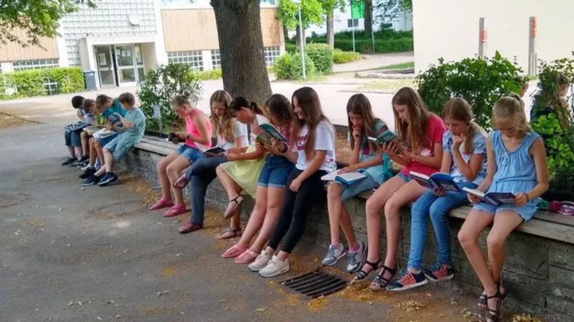 Leseauszeit auf dem Schulhof, Schüler sitzen lesend auf einer Mauer
