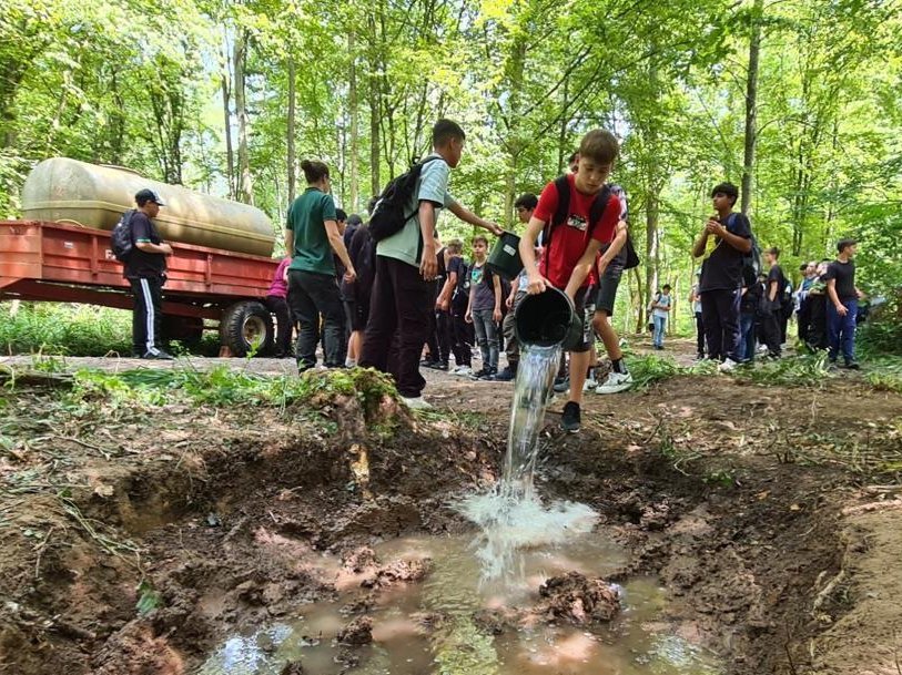 Schüler im Wald. Ein Schüler leert einen Eimer Wasser in eine Grube